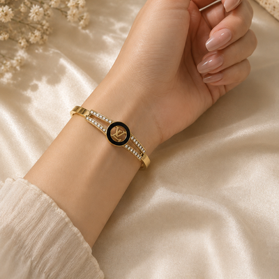 Hand wearing a LV gold bracelet with a black center on a soft beige background