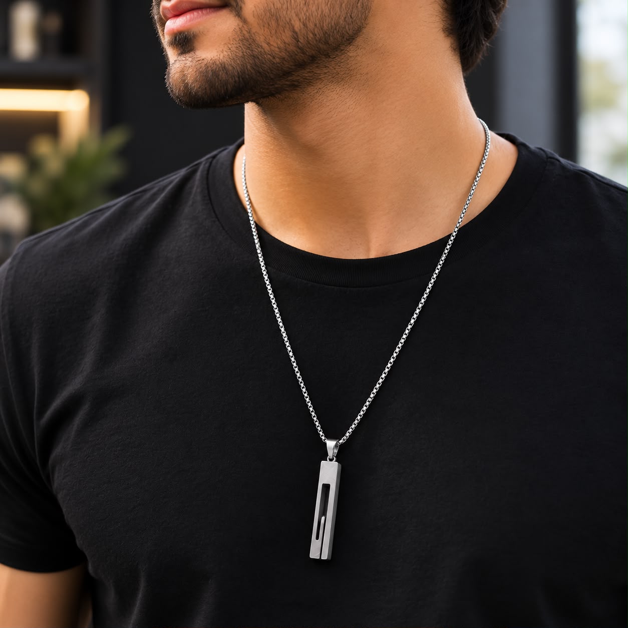 A man wearing a black t-shirt and a silver geometric pendant necklace, shown from the chest up.